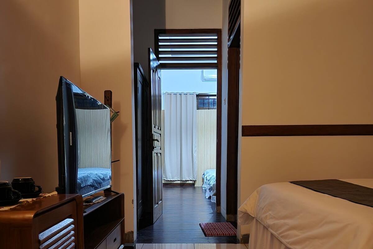 Hotellihuone, jossa on sänky, televisio, puinen lipasto ja kylpyhuone, joka näkyy avoimesta ovesta.