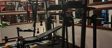 A gym with exercise equipment, mirrors, and a bench.