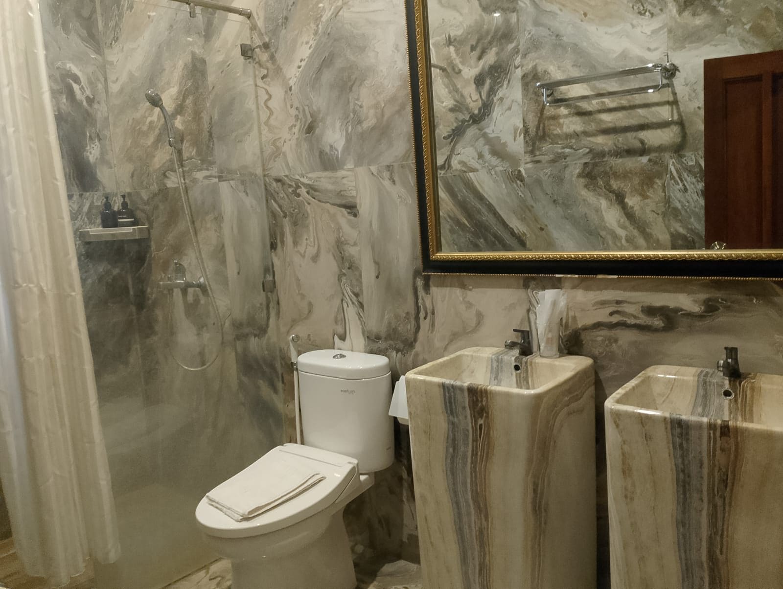 A bathroom with a marble wall, a toilet, a sink, and a shower.