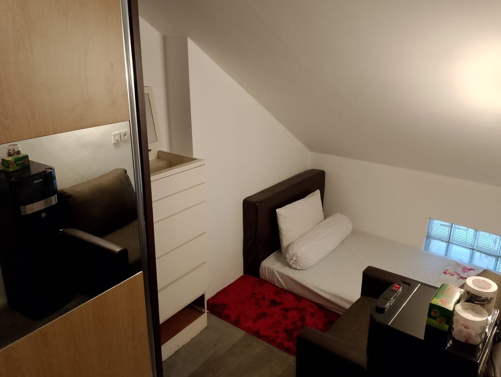 A small, modern bedroom with a bed, a dresser, a desk, and a window.