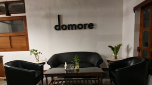 A modern room with a black leather sofa, a wooden coffee table, and two black armchairs. A wall-mounted sign reads "domore".