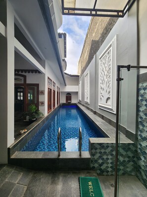 Une piscine entourée de parois en verre, un paillasson sur lequel est écrit « BIENVENUE », et une vue sur le ciel.