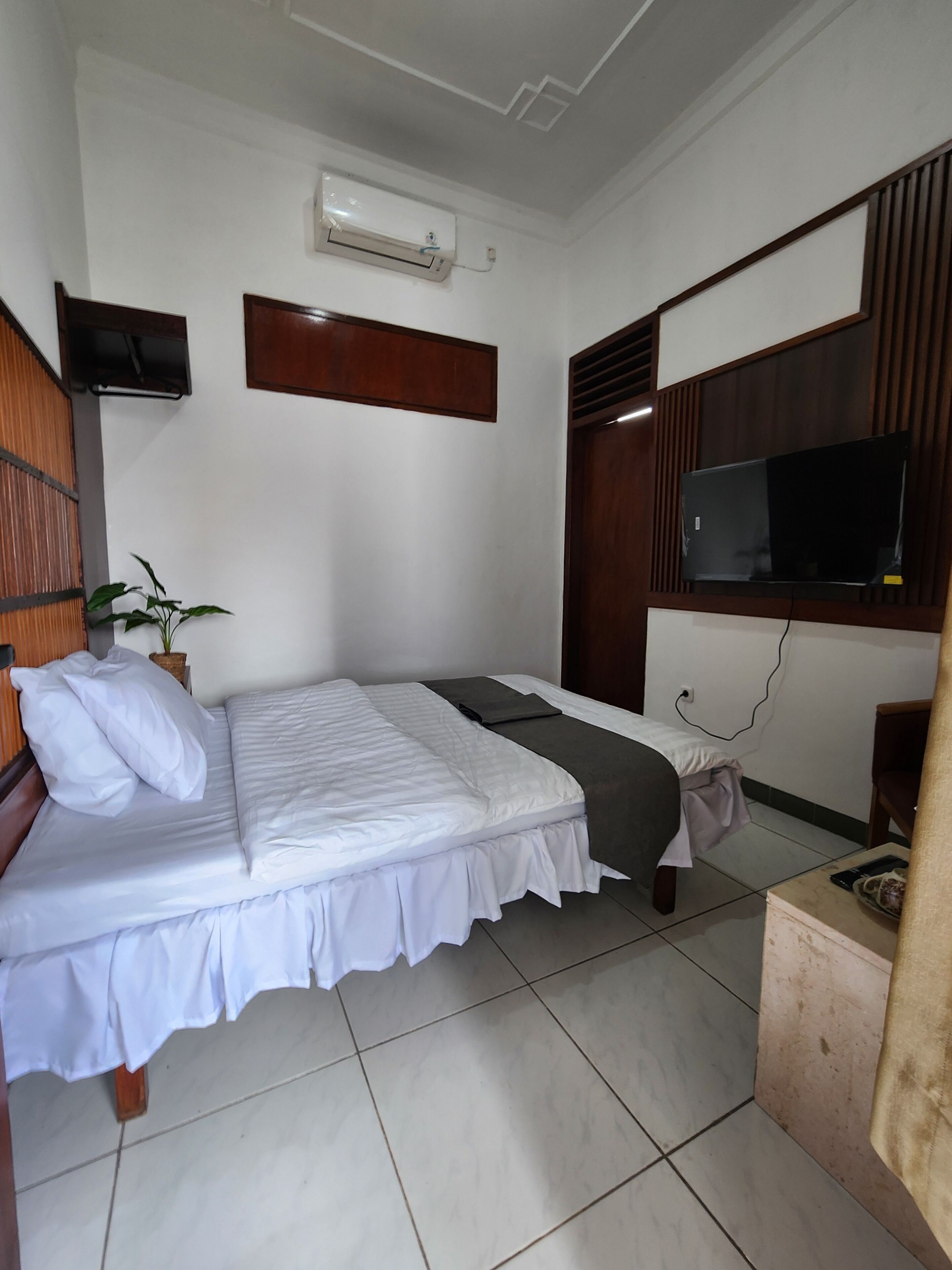 A neatly arranged bedroom with a bed, a television mounted on the wall, and a small table with a plant.