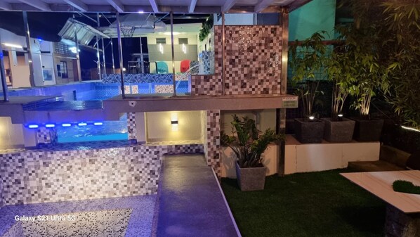 Un espace piscine extérieur moderne comprenant un terrain de basketball, un espace salon couvert et des plantes en pot.
