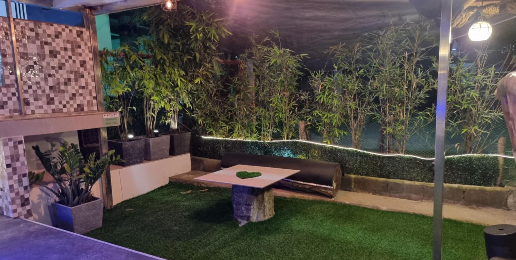 Un espace extérieur aménagé en terrasse, avec un revêtement de gazon synthétique, un coin salon et des plantes en pot.