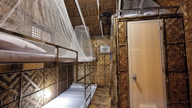 Une chambre avec des lits superposés, une armoire et un motif décoratif tissé sur le mur.