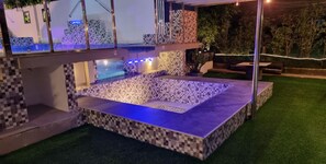 Un espace piscine extérieur moderne, doté d’un sol en mosaïque et d’un éclairage d’ambiance bleuté.