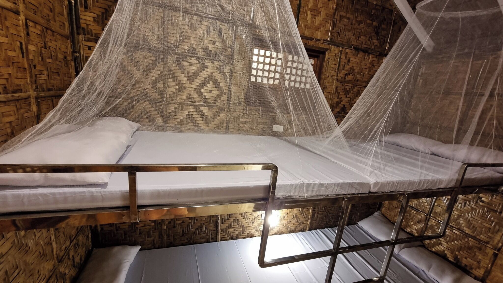 Una cama con mosquitero, paredes de madera y estructura metálica.
