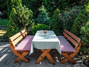 Un conjunto de banco y mesa de madera en un jardín con mantel a cuadros.