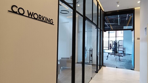 En modern inredning med en glasvägg där det står ”CO WORKING” och en hall som leder till ett träningsområde.