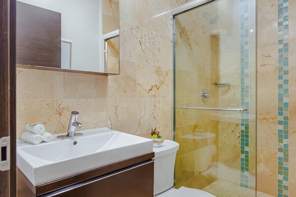 Un baño con lavamanos blanco, cabina de ducha de vidrio y pared con azulejos de mármol.