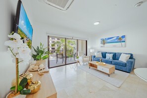 Uma sala de estar moderna com um sofá azul, uma mesa de centro e uma TV na parede.