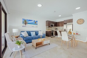 Uma sala de estar moderna com um sofá azul, uma mesa de centro e uma área de jantar com mesa e cadeiras de vidro.