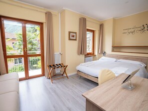 Una camera d'albergo con un letto, una scrivania, una sedia, un termosifone e una finestra con tende.