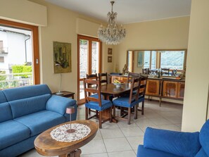 Een woonkamer met een blauwe bank, een houten salontafel en een eethoek met een houten tafel en stoelen.