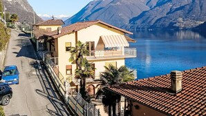 Un edificio de dos plantas con un balcón, una calle delante y un lago con montañas al fondo.