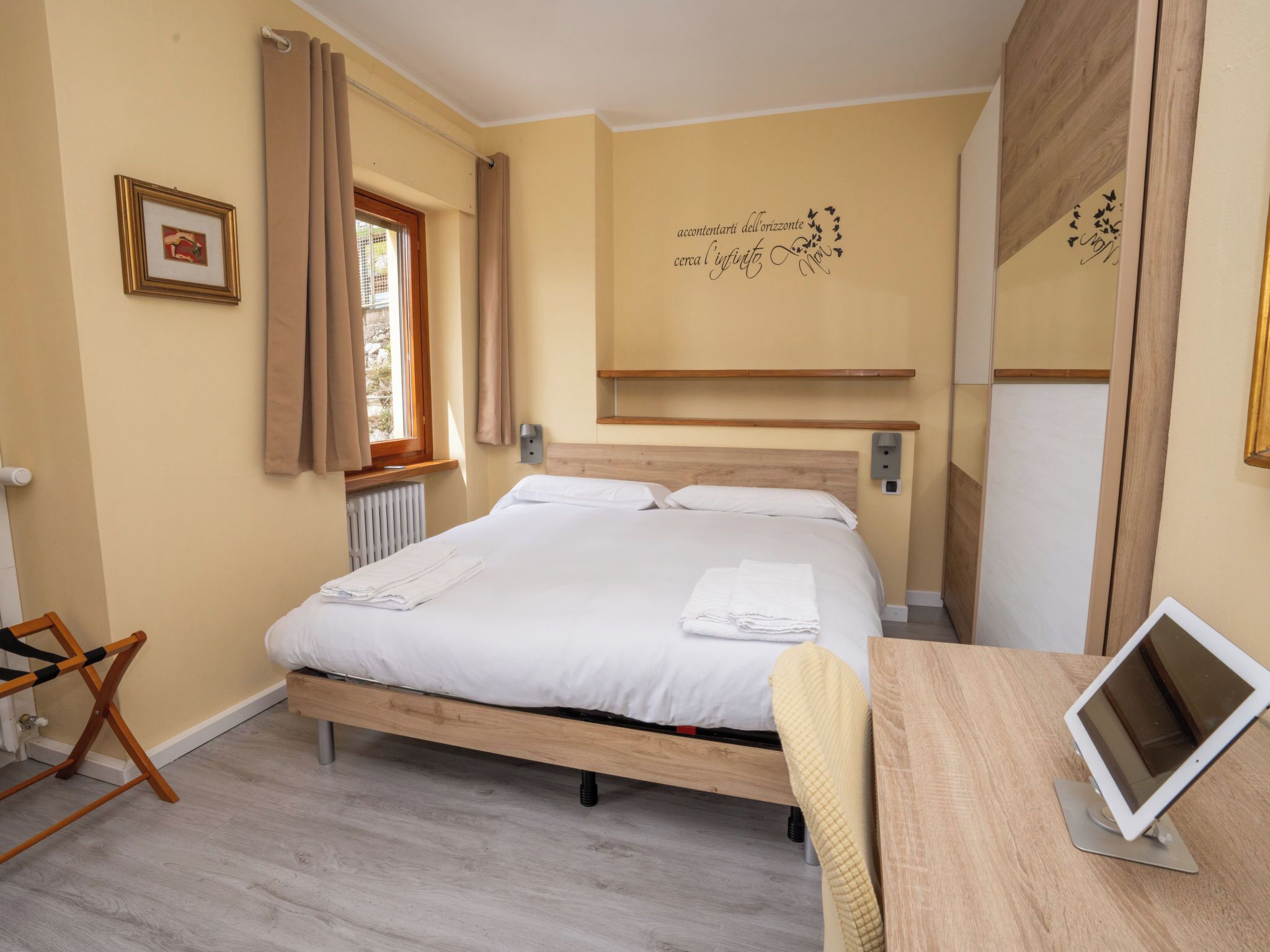 Ein Schlafzimmer mit einem Bett, einem Schreibtisch mit Computer, einem Heizkörper, einem Fenster mit Vorhängen und einer Wanddekoration.