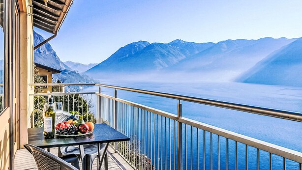 Un balcón con una mesa dispuesta para una comida, con vistas a un lago y montañas.