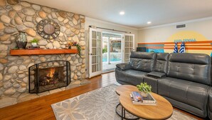 A living room with a stone fireplace, leather sofa, and a poolside view.