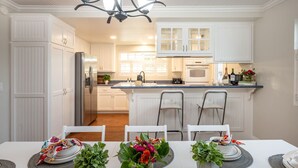 A modern kitchen with white cabinetry, a central island with bar stools, and a dining area with a white table set for a meal.