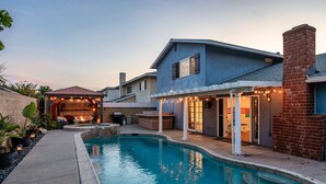 A residential swimming pool with a covered patio area, a barbecue setup, and a brick chimney.