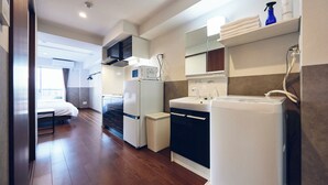 A modern kitchen with a microwave, refrigerator, and sink, a small trash bin, and a bed in the adjacent room. - MONTANA WING YEBISU (Osaka)