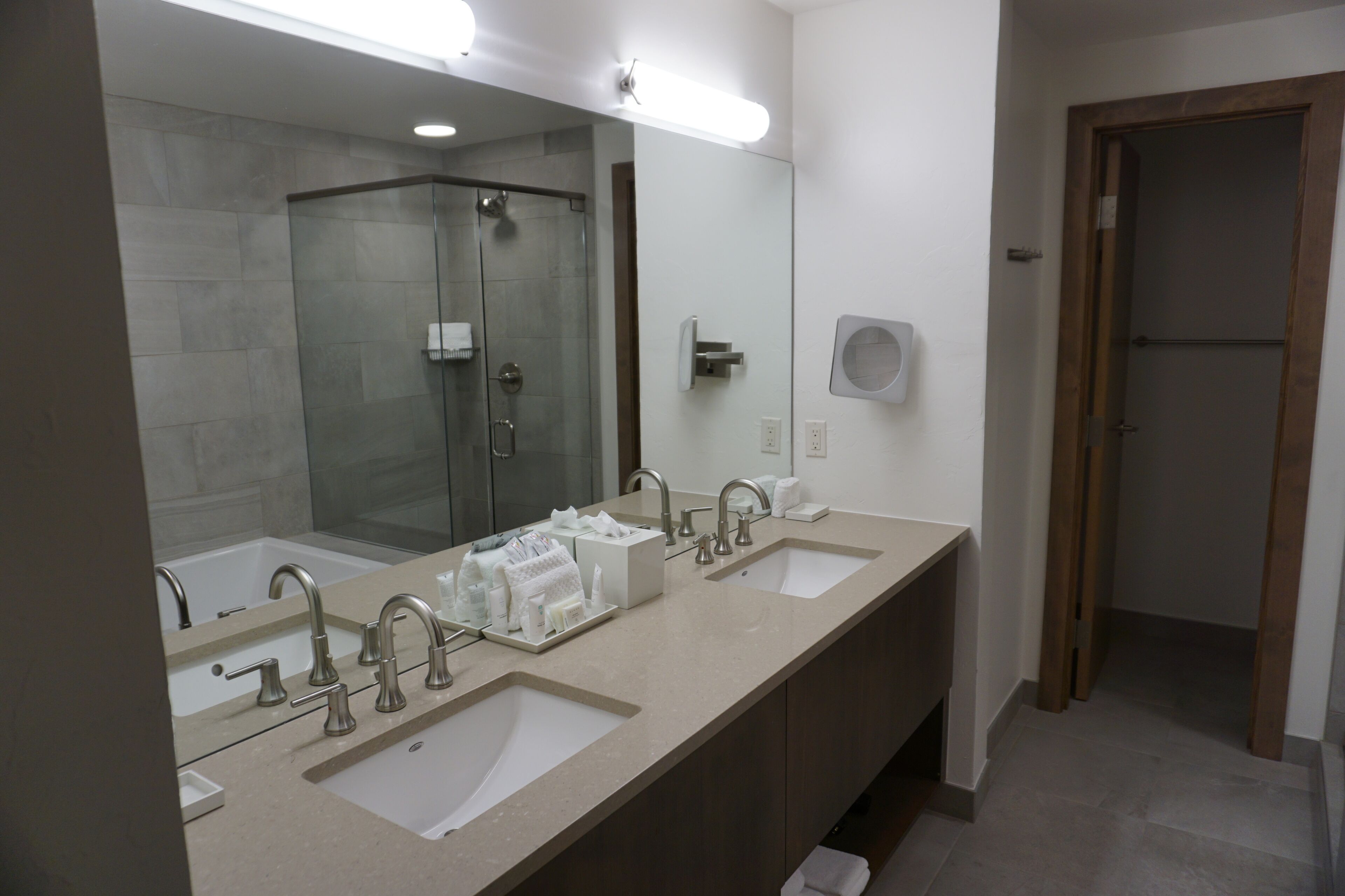 A modern bathroom with two sinks, a glass shower enclosure, and a large mirror.