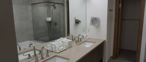A modern bathroom with two sinks, a glass shower enclosure, and a large mirror.