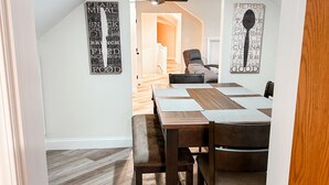 A dining area with a wooden table and chairs, a ceiling fan, and two wall art pieces.
