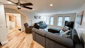 A spacious living room with a large sectional sofa, a television, and a ceiling fan.
