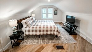 A bedroom with a checkered bedspread, a television, and a window with a view.