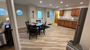 A spacious dining area with a round table and chairs, a kitchen with wooden cabinets, and a trash can. - Modern Riverbend Suites - 2BR (Bay City)