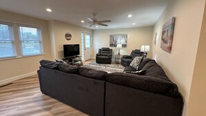 A modern living room with a sectional sofa, a flat-screen TV, and a ceiling fan. - Modern Riverbend Suites - 2BR (Bay City)