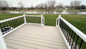 A wooden deck with white railings overlooking a grassy area with a body of water and houses in the background. - Modern Riverbend Suites - 2BR (Bay City)