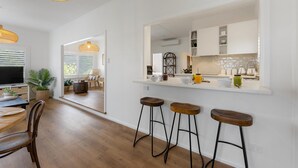 Una cocina moderna con armarios blancos, una isla grande con taburetes y un comedor con mesa y sillas de madera.