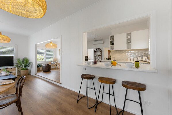 A modern kitchen with white cabinets, a large island with stools, and a dining area with a wooden table and chairs.
