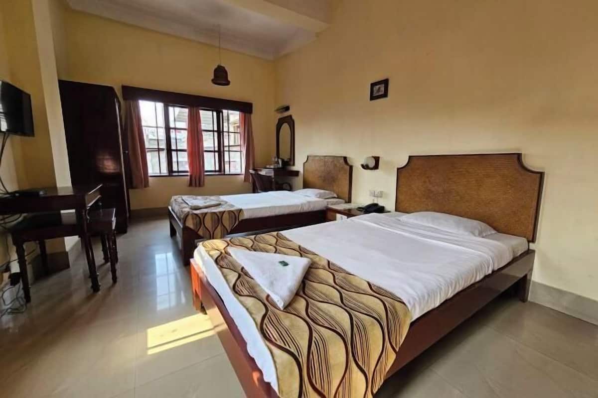 Quarto de hotel com duas camas, uma escrivaninha, uma cadeira, uma televisão e uma janela com cortinas.