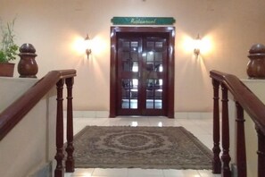A staircase leading to a restaurant with a wooden handrail, a patterned rug, and two wall-mounted lights. - Hotel Indsurya (Dibrugarh)