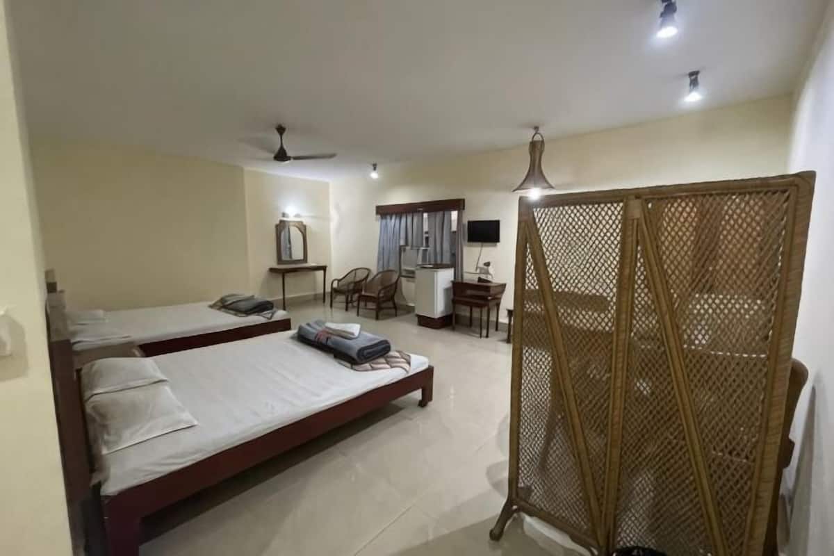 Quarto de hotel com duas camas, uma escrivaninha, uma cadeira, uma televisão e uma varanda com divisória de madeira.