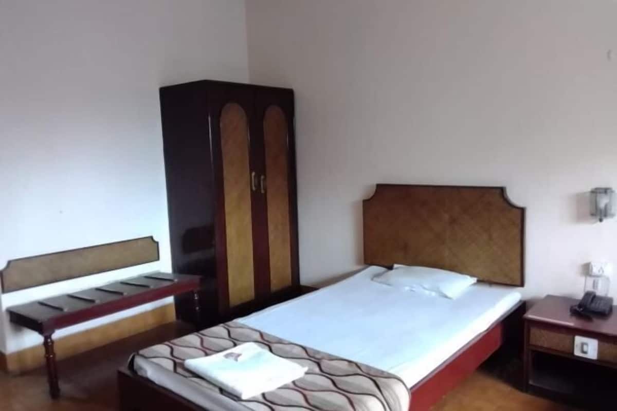 Quarto de hotel com cama, guarda-roupa, mesa de cabeceira e apoio para luminária.