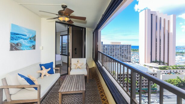 Un balcone con una ventola a soffitto, un divano con cuscini a forma di stella marina e vista su edifici alti e l'oceano.