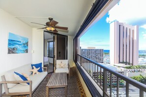 Un balcón con ventilador de techo, un sofá con almohadones de estrellas de mar y vistas a edificios altos y al océano.