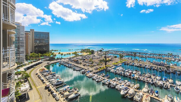 Un port de plaisance où sont amarrés de nombreux bateaux, un ciel bleu dégagé et une plage en arrière-plan.