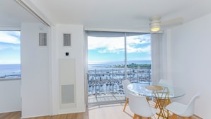 Un balcon avec une table et des chaises en verre, un ventilateur de plafond et une vue sur un port de plaisance.