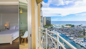 Un balcon avec un lit, une porte vitrée et une vue sur une marina avec des bateaux et une plage.