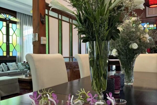 Un comedor con una mesa larga, sillas y un jarrón grande con flores.