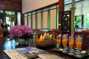 A dining table with a fruit basket, a floral arrangement, and three glasses of orange juice. - Luxurious Living by the River Hannah Villa (Chiang Mai)