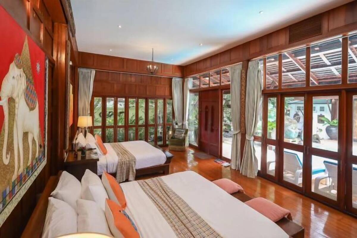A room with two beds, large windows, and a mural on the wall.