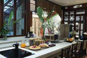 A kitchen with a dining area, featuring a countertop with food items, a coffee maker, and a refrigerator. - Luxurious Living by the River Hannah Villa (Chiang Mai)