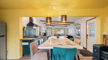 A modern kitchen with a central island, pendant lights, and a dining area with chairs.